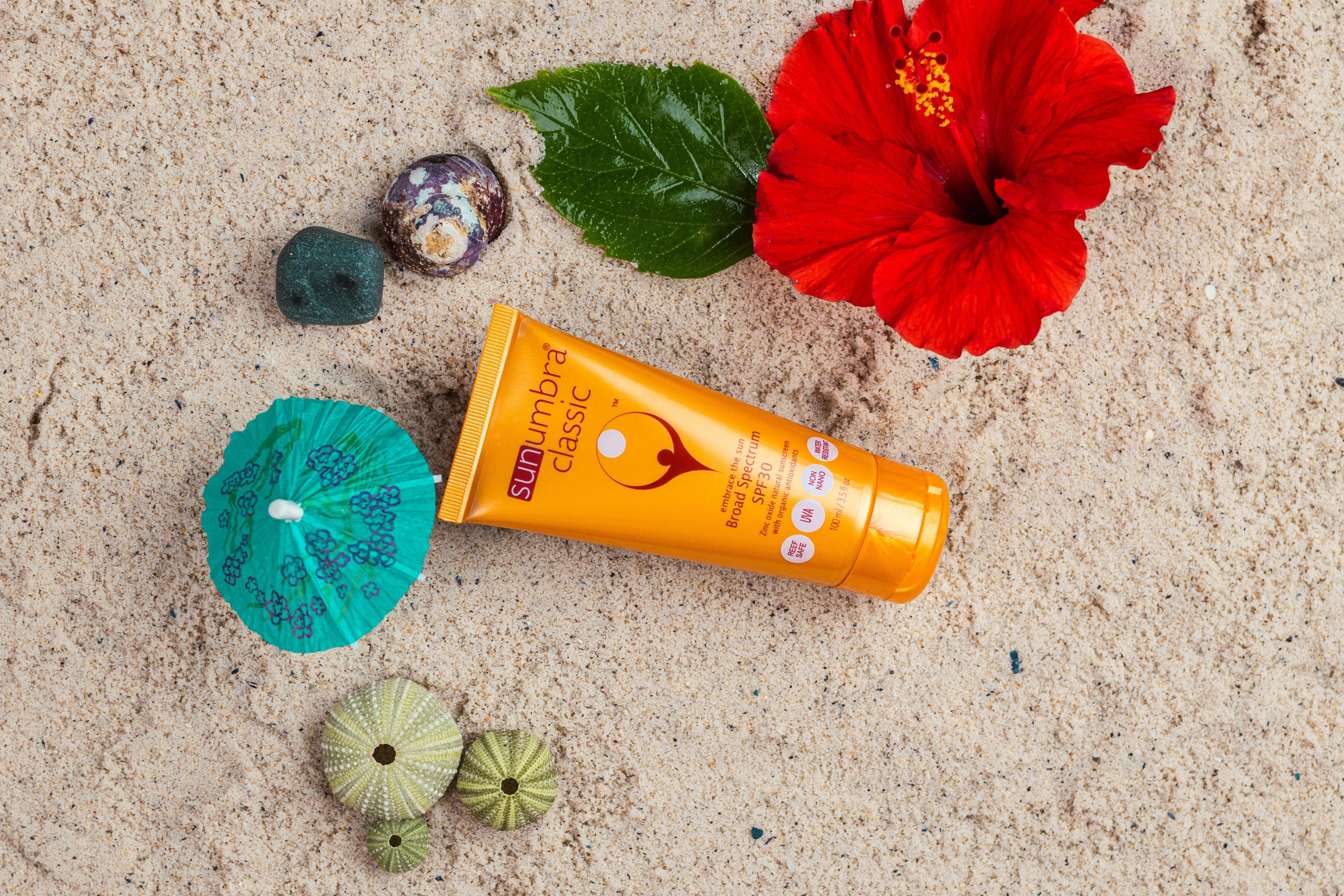 Sunscreen tube on sand with a red flower and green leaves